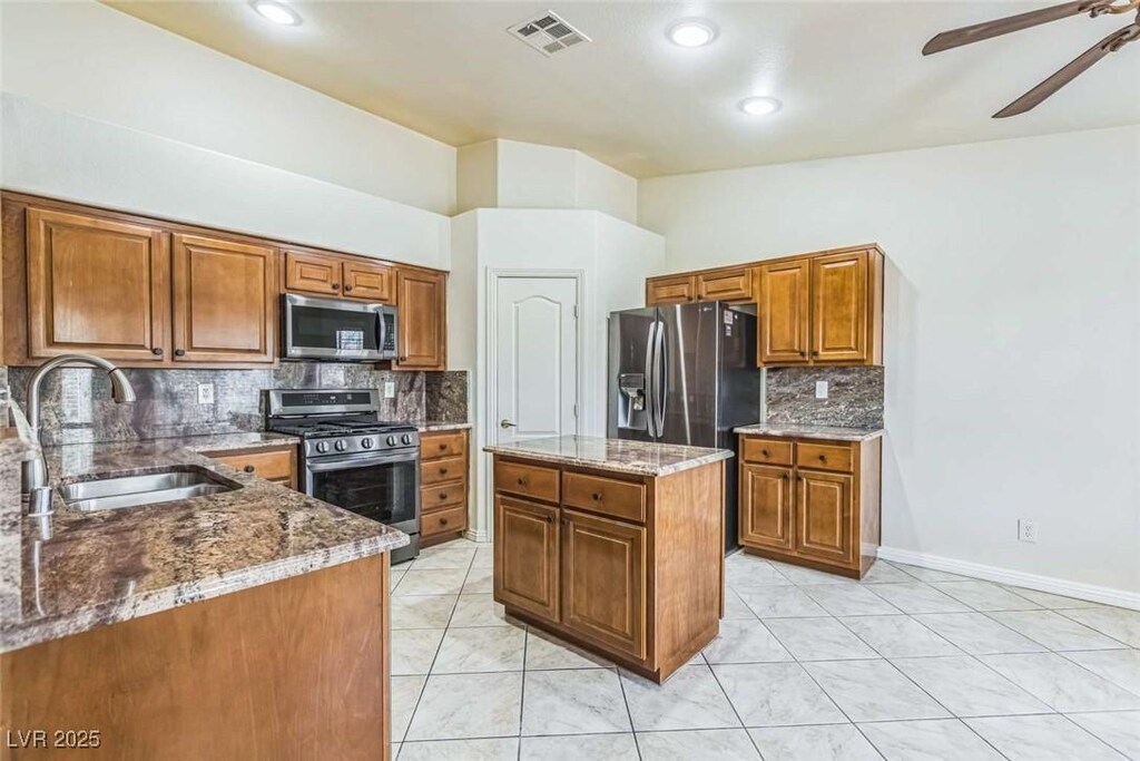3521 Amish Ave, North Las Vegas, NV 89031 - kitchen with appliances with stainless steel finishes, a sink, brown cabinetry, ceiling fan, and light stone counters