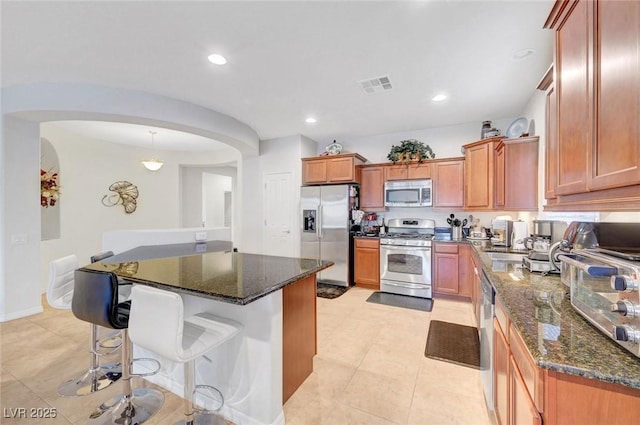 2613 Velodrome Ct, Henderson, NV 89044 - kitchen featuring stainless steel appliances, arched walkways, dark stone countertops, a kitchen bar, and recessed lighting