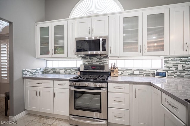 6417 Fisher Ave, Las Vegas, NV 89130 - kitchen with stainless steel appliances, decorative backsplash, white cabinets, light stone countertops, and glass insert cabinets