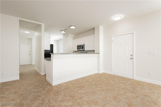 3041 Gary Cooper St Unit 103, Las Vegas, NV 89122 - kitchen featuring stainless steel microwave, white cabinets, a peninsula, black refrigerator, and light tile patterned floors