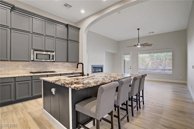 8544 Garden Valley Ct, Las Vegas, NV 89178 - kitchen with a sink, stainless steel appliances, arched walkways, light stone counters, and light wood-type flooring