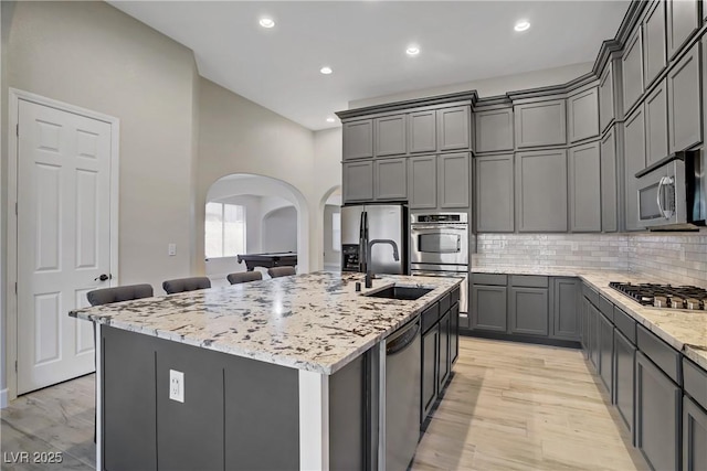 8544 Garden Valley Ct, Las Vegas, NV 89178 - kitchen with arched walkways, appliances with stainless steel finishes, a sink, light stone counters, and gray cabinets