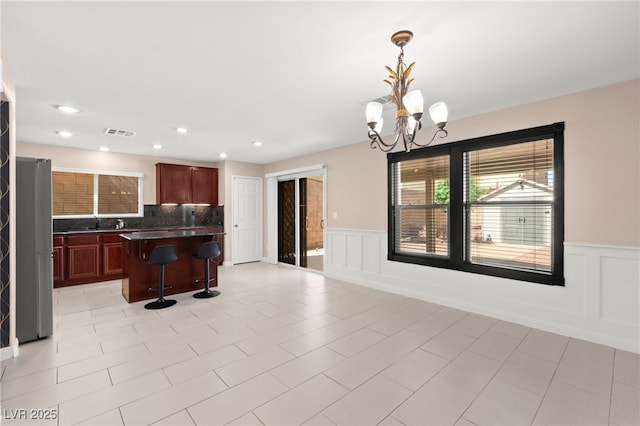 11755 Garland Grove Ln, Las Vegas, NV 89183 - kitchen featuring dark countertops, a breakfast bar area, a chandelier, a wainscoted wall, and a center island