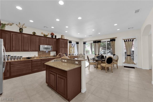 6739 Quapaw St, Las Vegas, NV 89149 - kitchen featuring appliances with stainless steel finishes, a sink, a center island with sink, light stone counters, and backsplash