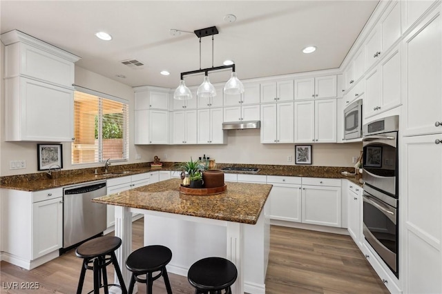 11707 Longworth Rd, Las Vegas, NV 89135 - kitchen with stainless steel appliances, a breakfast bar area, wood finished floors, under cabinet range hood, and white cabinets
