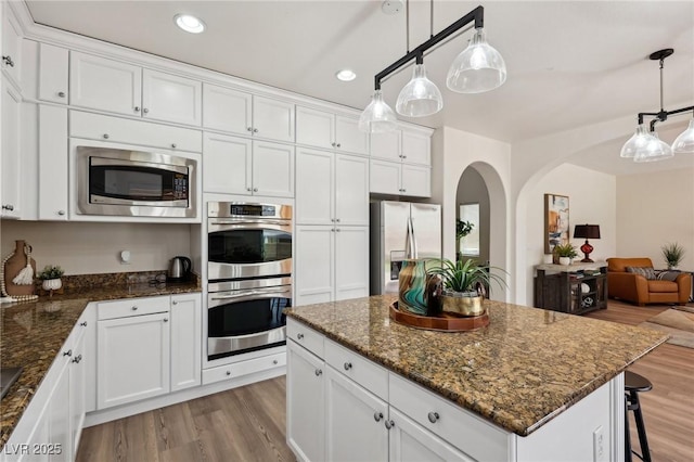 11707 Longworth Rd, Las Vegas, NV 89135 - kitchen with appliances with stainless steel finishes, wood finished floors, arched walkways, open floor plan, and white cabinets