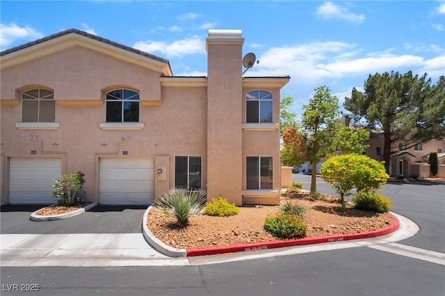 3950 S Sandhill Rd Unit 130, Las Vegas, NV 89121 - view of front of home with stucco siding, driveway, a garage, and a chimney