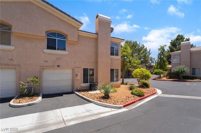 3950 S Sandhill Rd Unit 130, Las Vegas, NV 89121 - view of front facade with an attached garage, stucco siding, driveway, and a chimney