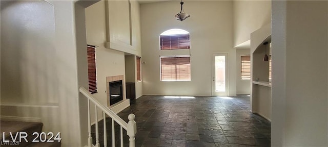 4821 Whisper Lake Ave, Las Vegas, NV 89131 - unfurnished living room featuring stone tile floors, a towering ceiling, a glass covered fireplace, and baseboards