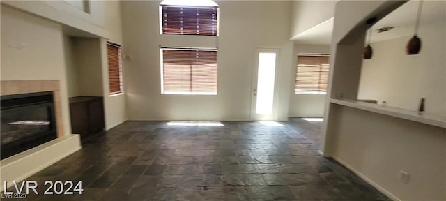 4821 Whisper Lake Ave, Las Vegas, NV 89131 - unfurnished living room with healthy amount of natural light, stone tile flooring, a high ceiling, a fireplace with raised hearth, and baseboards