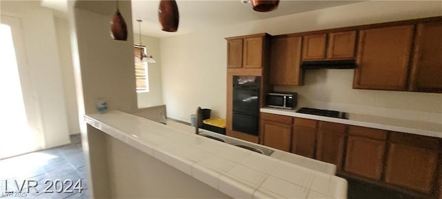 4821 Whisper Lake Ave, Las Vegas, NV 89131 - kitchen featuring brown cabinetry, black appliances, under cabinet range hood, and pendant lighting