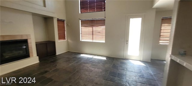 4821 Whisper Lake Ave, Las Vegas, NV 89131 - unfurnished living room with stone tile flooring, a glass covered fireplace, a high ceiling, and baseboards