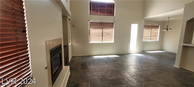 4821 Whisper Lake Ave, Las Vegas, NV 89131 - unfurnished living room featuring stone tile floors, a glass covered fireplace, a chandelier, baseboards, and a high ceiling