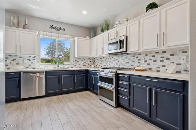 2425 Sturrock Dr, Henderson, NV 89044 - kitchen featuring stainless steel appliances, white cabinetry, a sink, blue cabinets, and decorative backsplash