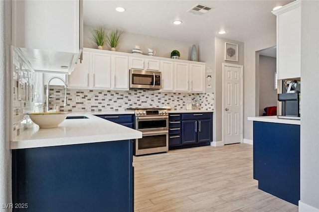 2425 Sturrock Dr, Henderson, NV 89044 - kitchen featuring stainless steel appliances, blue cabinetry, backsplash, light wood-type flooring, and white cabinets