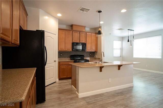 7715 Peaceful Trellis Dr, Las Vegas, NV 89179 - kitchen featuring black appliances, a sink, light wood-type flooring, a kitchen island with sink, and a breakfast bar