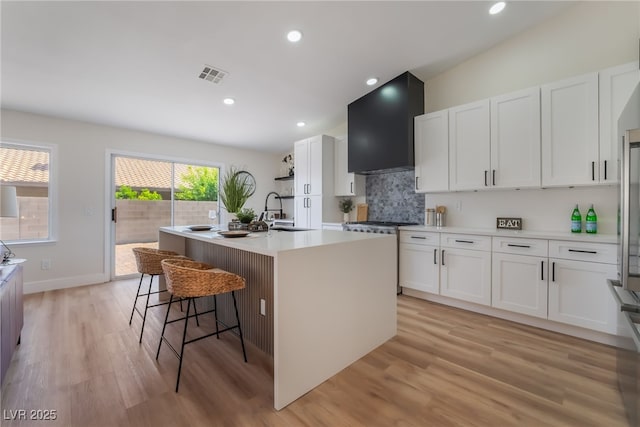 9705 Standard Ave, Las Vegas, NV 89129 - kitchen featuring a sink, gas range, wall chimney range hood, an island with sink, and white cabinetry