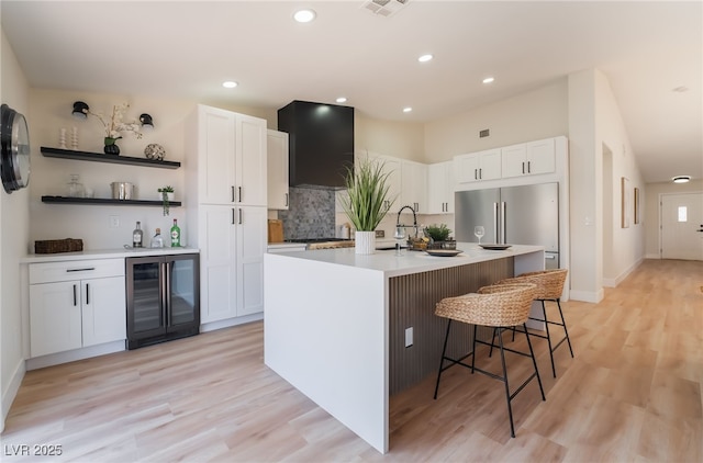 9705 Standard Ave, Las Vegas, NV 89129 - kitchen with beverage cooler, a breakfast bar area, a center island with sink, white cabinets, and light wood-style floors
