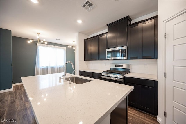 871 Aurelie Ridge St, Henderson, NV 89011 - kitchen featuring appliances with stainless steel finishes, a sink, dark wood-style flooring, a center island with sink, and decorative backsplash