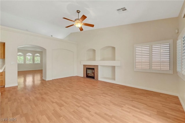 4197 Bottiglia Ave, Las Vegas, NV 89141 - unfurnished living room with light wood-style flooring, a ceiling fan, a tile fireplace, lofted ceiling, and arched walkways