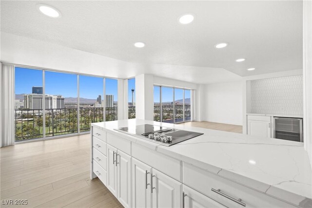 3111 Bel Air Dr Unit 24G, Las Vegas, NV 89109 - kitchen with black electric stovetop, beverage cooler, white cabinetry, a city view, and light stone countertops