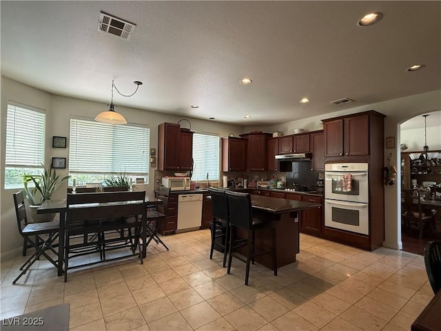 11457 Steponia Bay St, Las Vegas, NV 89141 - kitchen featuring white appliances, dark countertops, a kitchen island, recessed lighting, and arched walkways