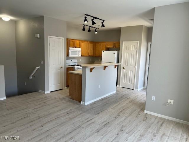 6170 E Sahara Ave Unit 1012, Las Vegas, NV 89142 - kitchen with white appliances, rail lighting, light countertops, a breakfast bar, and light wood-style flooring