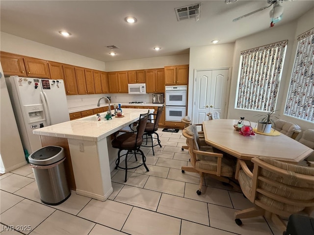 6351 Davidson Ct, Las Vegas, NV 89110 - kitchen with white appliances, a breakfast bar area, brown cabinetry, a sink, and recessed lighting