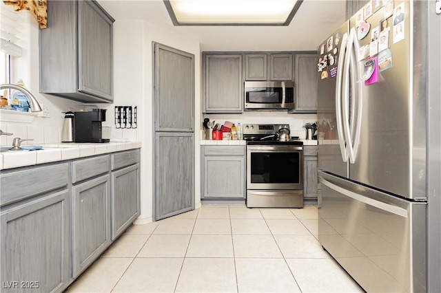 2251 Bridger St, Pahrump, NV 89048 - kitchen with appliances with stainless steel finishes, tile counters, gray cabinetry, and light tile patterned floors