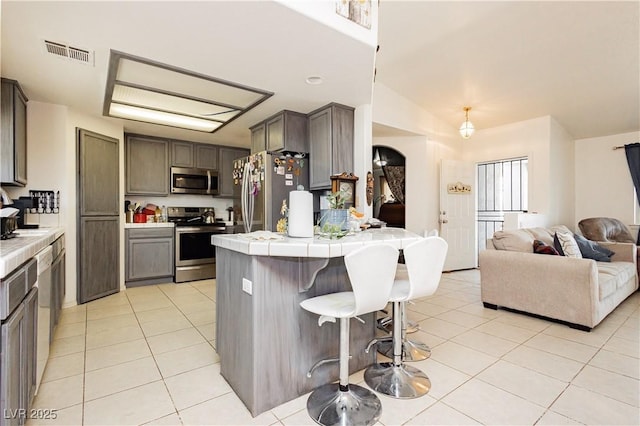 2251 Bridger St, Pahrump, NV 89048 - kitchen with stainless steel appliances, tile counters, light tile patterned floors, a kitchen bar, and a peninsula