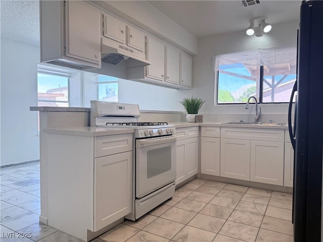 5600 Grossmont Ave, Las Vegas, NV 89110 - kitchen featuring white range with gas stovetop, under cabinet range hood, freestanding refrigerator, a sink, and a peninsula