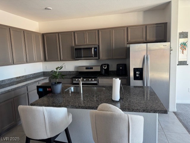 411 Hellebores Ave, North Las Vegas, NV 89084 - kitchen with stainless steel appliances, a sink, dark stone counters, a breakfast bar area, and light tile patterned floors