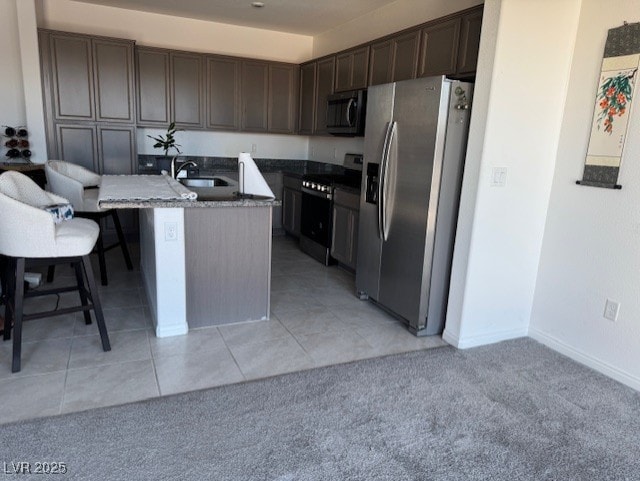 411 Hellebores Ave, North Las Vegas, NV 89084 - kitchen with appliances with stainless steel finishes, a sink, dark brown cabinetry, a kitchen island with sink, and light tile patterned floors