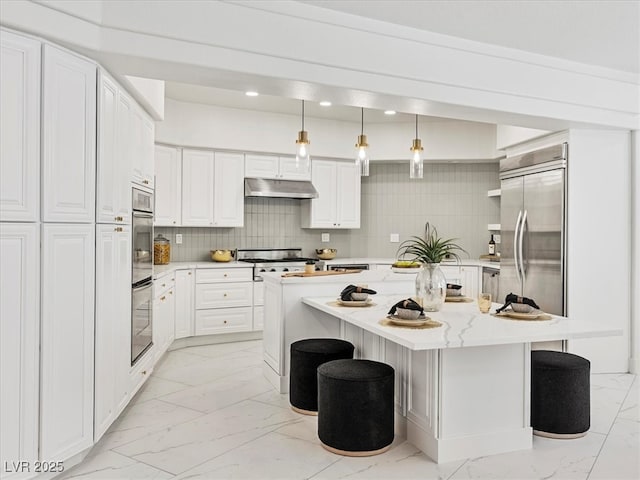21 Sawgrass Ct, Las Vegas, NV 89113 - kitchen with light marble finish flooring, under cabinet range hood, appliances with stainless steel finishes, white cabinetry, and a center island