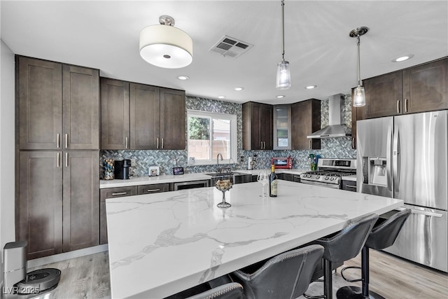 9585 Teton Diablo Ave, Las Vegas, NV 89117 - kitchen featuring appliances with stainless steel finishes, wall chimney range hood, dark brown cabinets, a breakfast bar, and light wood finished floors