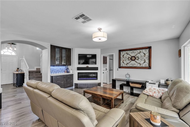 9585 Teton Diablo Ave, Las Vegas, NV 89117 - living room with arched walkways, a glass covered fireplace, light wood-style floors, and stairway