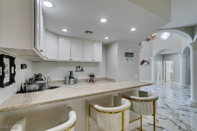 2101 Diamond Bar Dr, Las Vegas, NV 89117 - kitchen featuring ornate columns, light marble finish floors, arched walkways, white cabinetry, and a kitchen breakfast bar