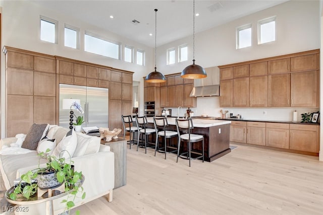 5155 Rock Daisy Dr, Las Vegas, NV 89135 - kitchen with a towering ceiling, a breakfast bar area, light wood-style flooring, stainless steel appliances, and wall chimney exhaust hood
