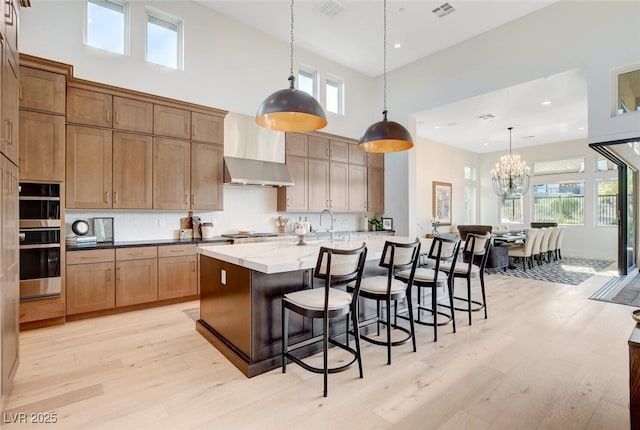 5155 Rock Daisy Dr, Las Vegas, NV 89135 - kitchen featuring wall chimney range hood, a towering ceiling, stainless steel double oven, light wood-type flooring, and a chandelier