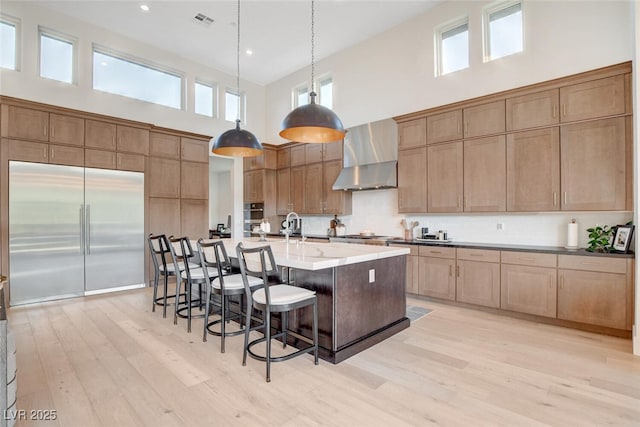 5155 Rock Daisy Dr, Las Vegas, NV 89135 - kitchen with wall chimney range hood, stainless steel appliances, a high ceiling, light wood-style floors, and a kitchen bar