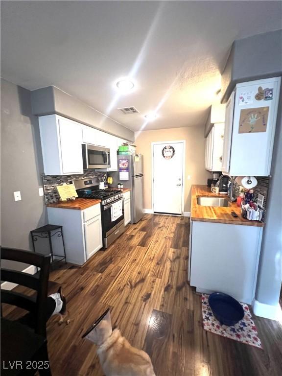 779 Peregrine Falcon St, Henderson, NV 89015 - kitchen with appliances with stainless steel finishes, wood counters, a sink, dark wood finished floors, and decorative backsplash