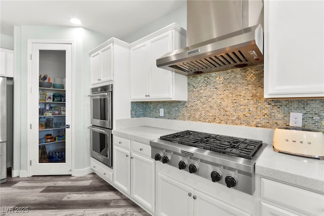 424 Vigo Port St, Las Vegas, NV 89138 - kitchen with wall chimney exhaust hood, appliances with stainless steel finishes, wood finished floors, white cabinetry, and tasteful backsplash