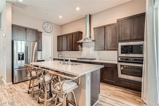 2507 Silent View Ave, Henderson, NV 89044 - kitchen with stainless steel appliances, a sink, wall chimney range hood, dark brown cabinetry, and light countertops