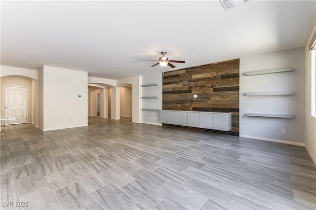 7265 Southern Magnolia St, Las Vegas, NV 89149 - unfurnished living room with arched walkways, a ceiling fan, wood walls, an accent wall, and baseboards