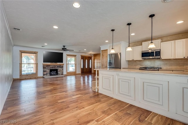 7950 Red Barn Dr, Las Vegas, NV 89123 - kitchen featuring stainless steel appliances, ceiling fan, a fireplace, tasteful backsplash, and light wood-type flooring