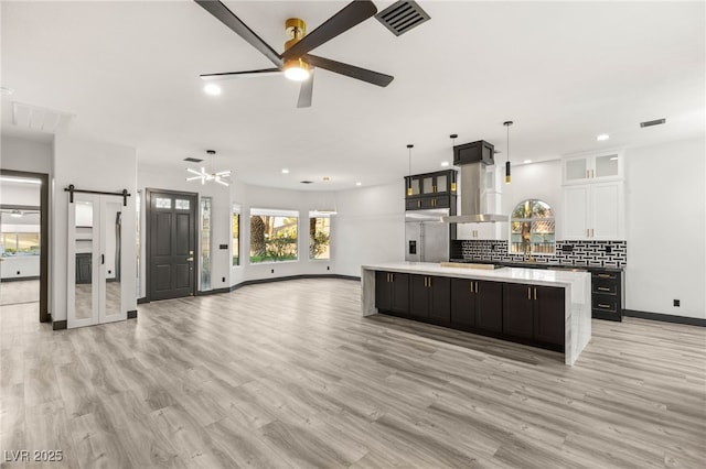 9029 Rivers Edge Dr, Las Vegas, NV 89117 - kitchen featuring a barn door, a spacious island, ceiling fan, wall chimney range hood, and white cabinets