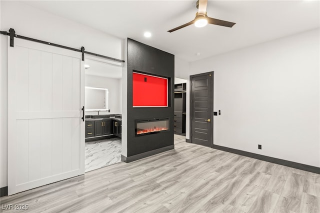 9029 Rivers Edge Dr, Las Vegas, NV 89117 - unfurnished bedroom featuring a barn door, light wood-style flooring, a glass covered fireplace, ensuite bath, and recessed lighting