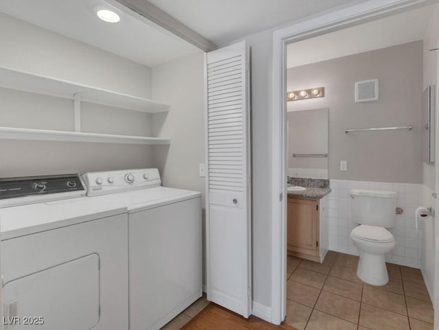 7950 W Flamingo Rd Unit 1077, Las Vegas, NV 89147 - laundry area featuring separate washer and dryer, light tile patterned floors, tile walls, and a wainscoted wall
