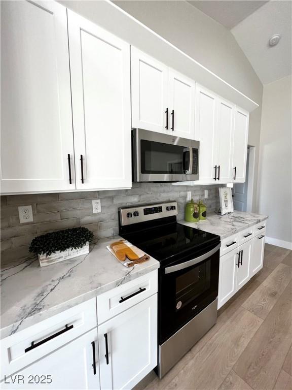 3791 Soplo Rd, Pahrump, NV 89048 - kitchen with stainless steel appliances, light wood-type flooring, white cabinets, light stone countertops, and vaulted ceiling