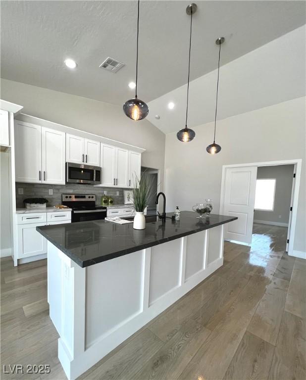 3791 Soplo Rd, Pahrump, NV 89048 - kitchen featuring stainless steel appliances, lofted ceiling, light wood finished floors, white cabinetry, and dark countertops